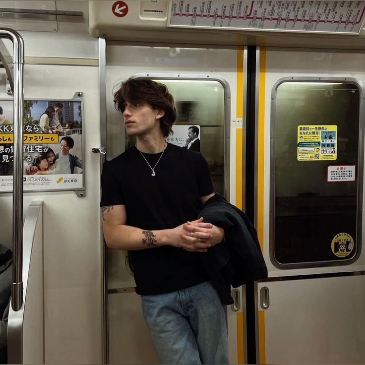 a man standing on a subway train with his arms crossed and looking off to the side