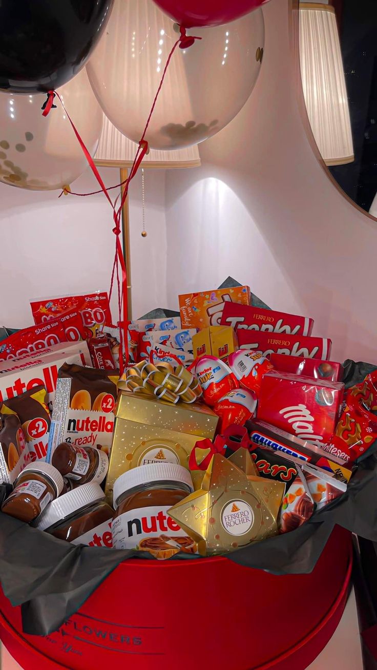 a red bucket filled with lots of candy and chocolates next to a balloon in the shape of a heart