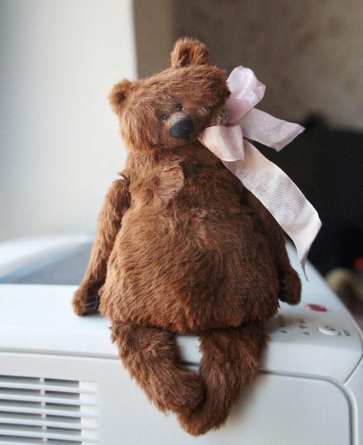 a brown teddy bear sitting on top of an air conditioner with a pink bow