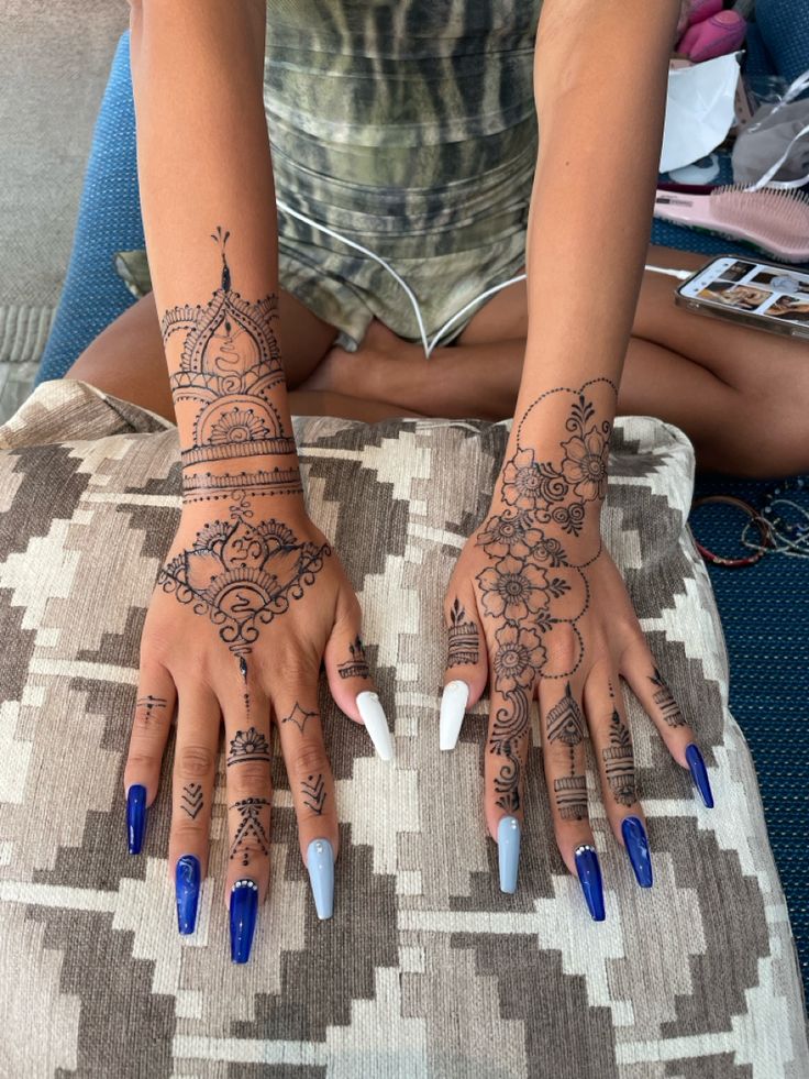 two hands with blue and white nail polishes on them, sitting on a cushion