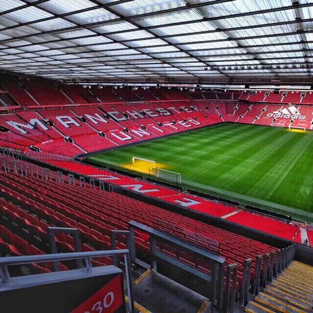 the inside of an empty stadium with red seats and green field in front of it