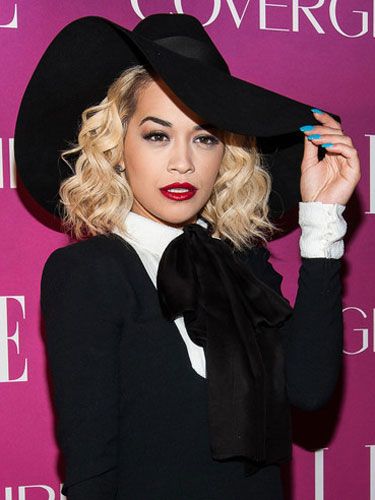 a woman in a black hat and dress posing for the camera with her hand on her hip