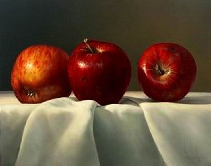 three red apples sitting on top of a white table cloth next to an apple painting