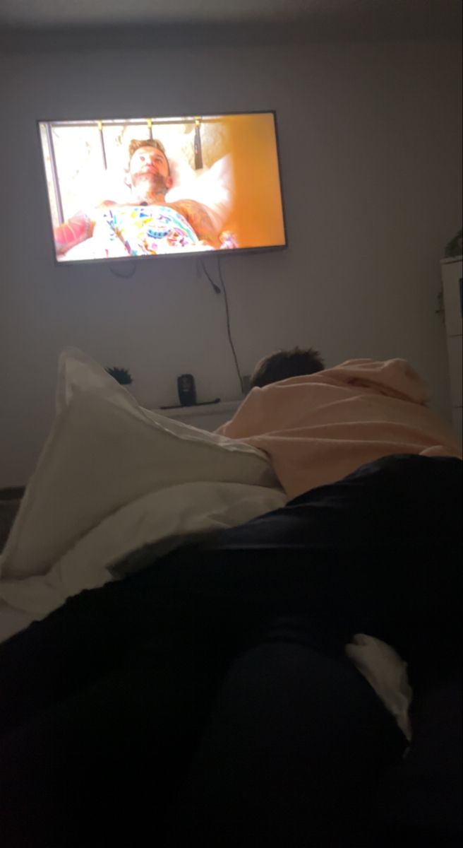 a person laying in bed watching television on the wall above them is a large flat screen tv