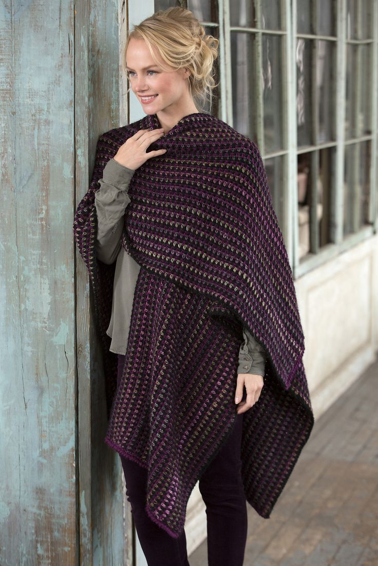 a woman standing next to a wooden door wearing a purple and black ponchle