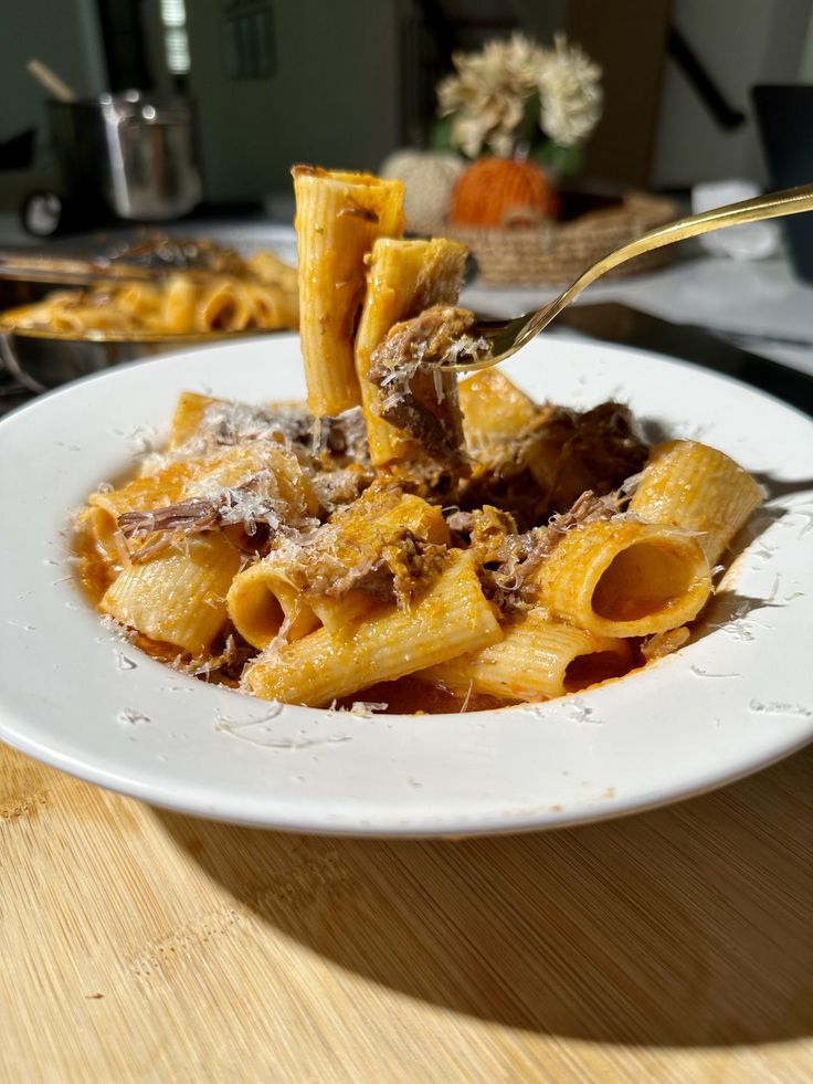 a white plate topped with pasta covered in sauce and meat next to a fork on top of a wooden table