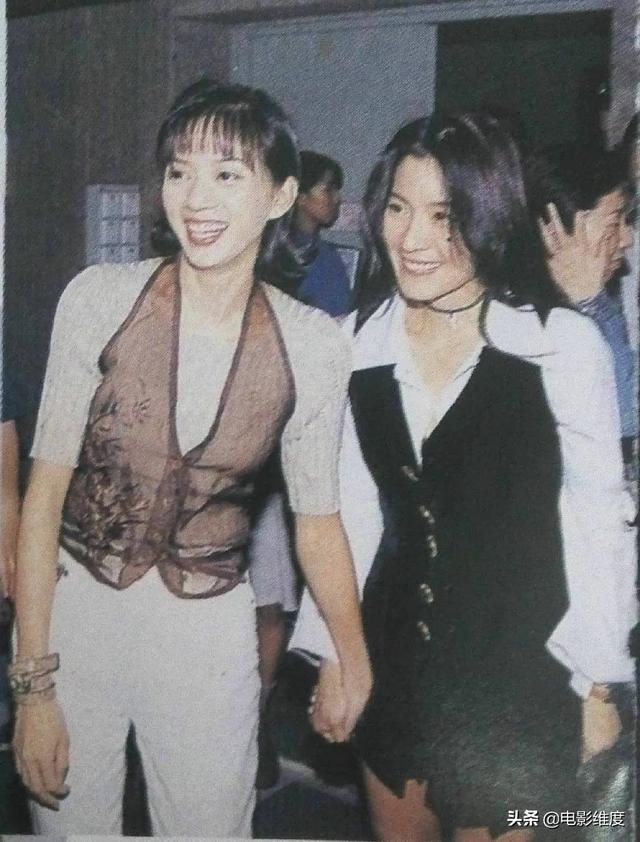 an old photo of two women holding hands and smiling at the camera with people in the background