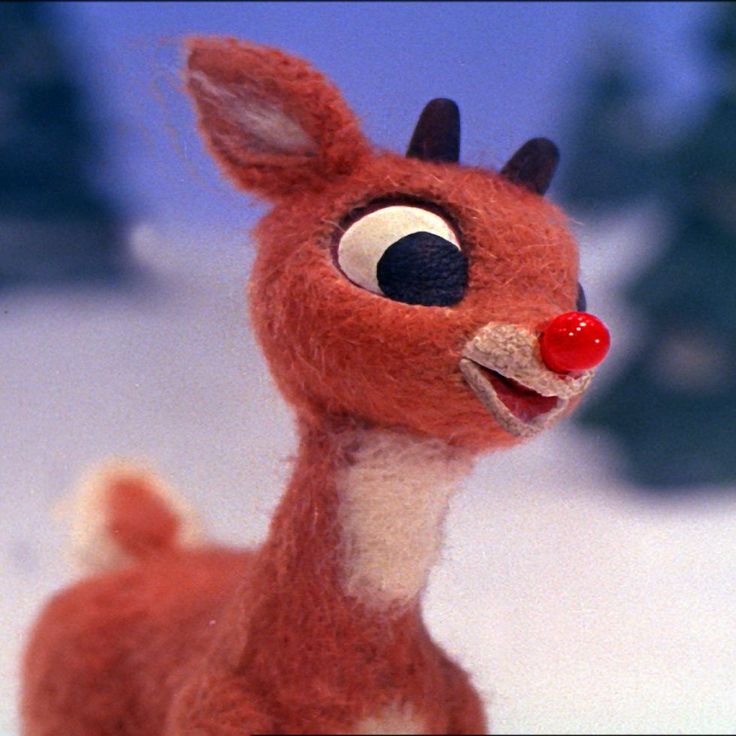 a close up of a stuffed animal on a snow covered ground with trees in the background