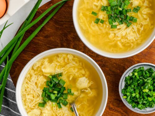 two white bowls filled with soup next to green onions and an egg on the side