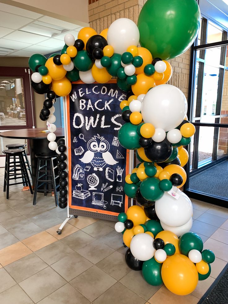 a welcome sign made out of balloons in the shape of an arch with green, white and yellow balloons