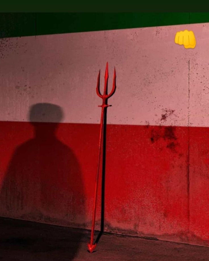 the shadow of a person standing next to a red and white wall with two pitchforks