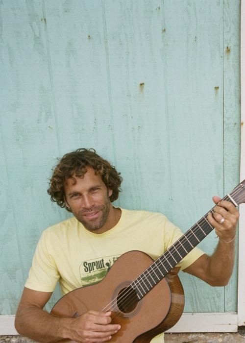 a man is holding an acoustic guitar in front of a blue door and smiling at the camera