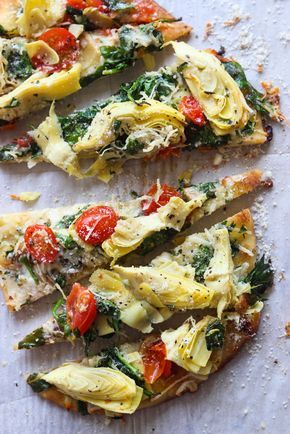 two slices of pizza with tomatoes, spinach and cheese on them sitting on a piece of parchment paper