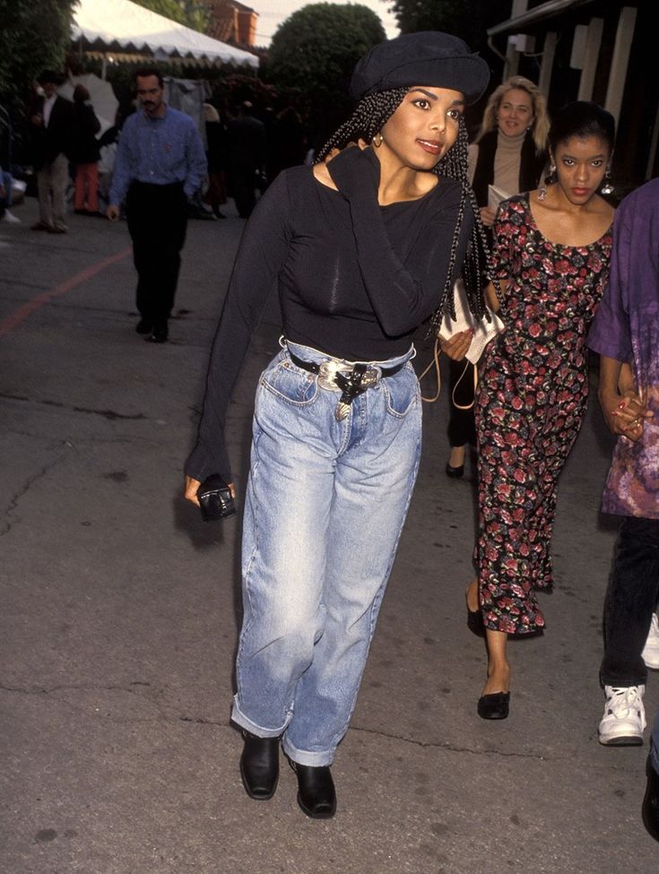 a woman walking down the street with her hand in her pocket and wearing black hat