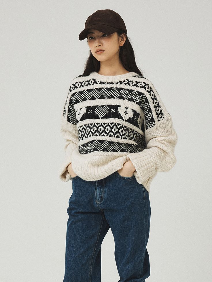 a woman wearing jeans and a sweater stands in front of a white background