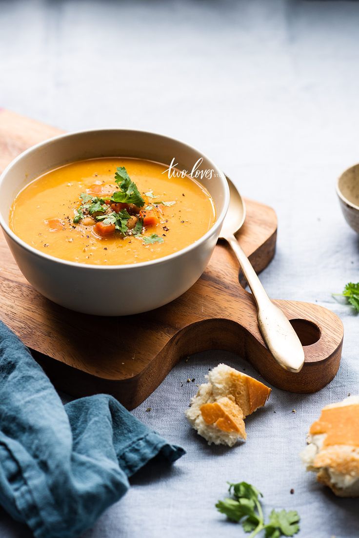 a bowl of soup on a cutting board with bread and garnishes next to it