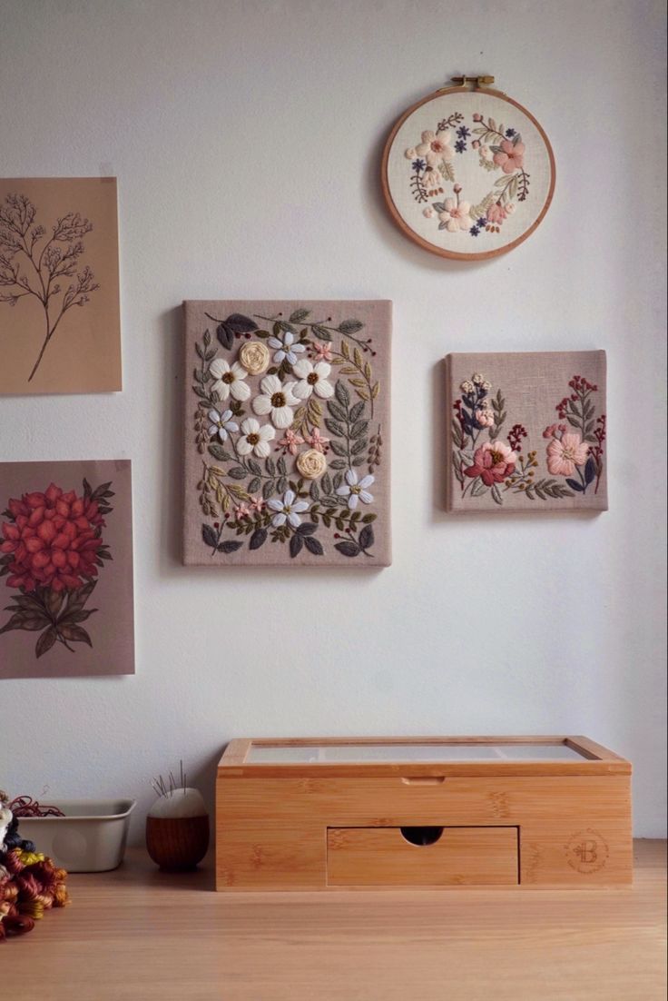 three floral paintings hang on the wall next to a wooden chest with drawers underneath it