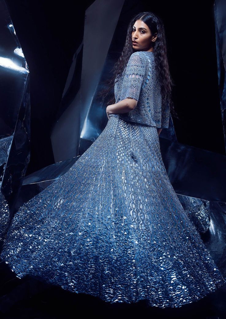 a woman in a blue dress standing next to some shiny metal foils and looking off into the distance