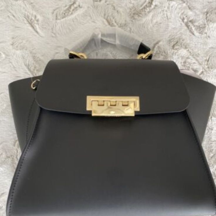 New Zac Zac Posen Women's Eartha Iconic Soft Top Handle Satchel Bag - Black. New With Tags The Eartha Top Handle Crossbody Bag Is A Medium Sized Carry All With Signature Winged Panels And Gleaming Polished Hardware For A Glamorous Finish. - Single Top Handle - Detachable Shoulder Strap Foldover Flap With Flip Lock Closure - Exterior Features Leather Construction, Back Slip Pocket - Interior Features Wall Slip Pocket - Approx. 8" H X 9" W X 5" D - Approx. 3" Handle Drop, 22" Shoulder Strap High-end Tan Bags For Office, High-end Tan Office Bags, Designer Tan Satchel, Light Luxury Evening Crossbody Bag, Light Luxury Gold-tone Satchel For Shopping, Light Luxury Gold-tone Hardware Satchel For Shopping, Designer Gold Satchel For Formal Occasions, Light Luxury Formal Crossbody Bag, Light Luxury Crossbody Bag For Formal Occasions