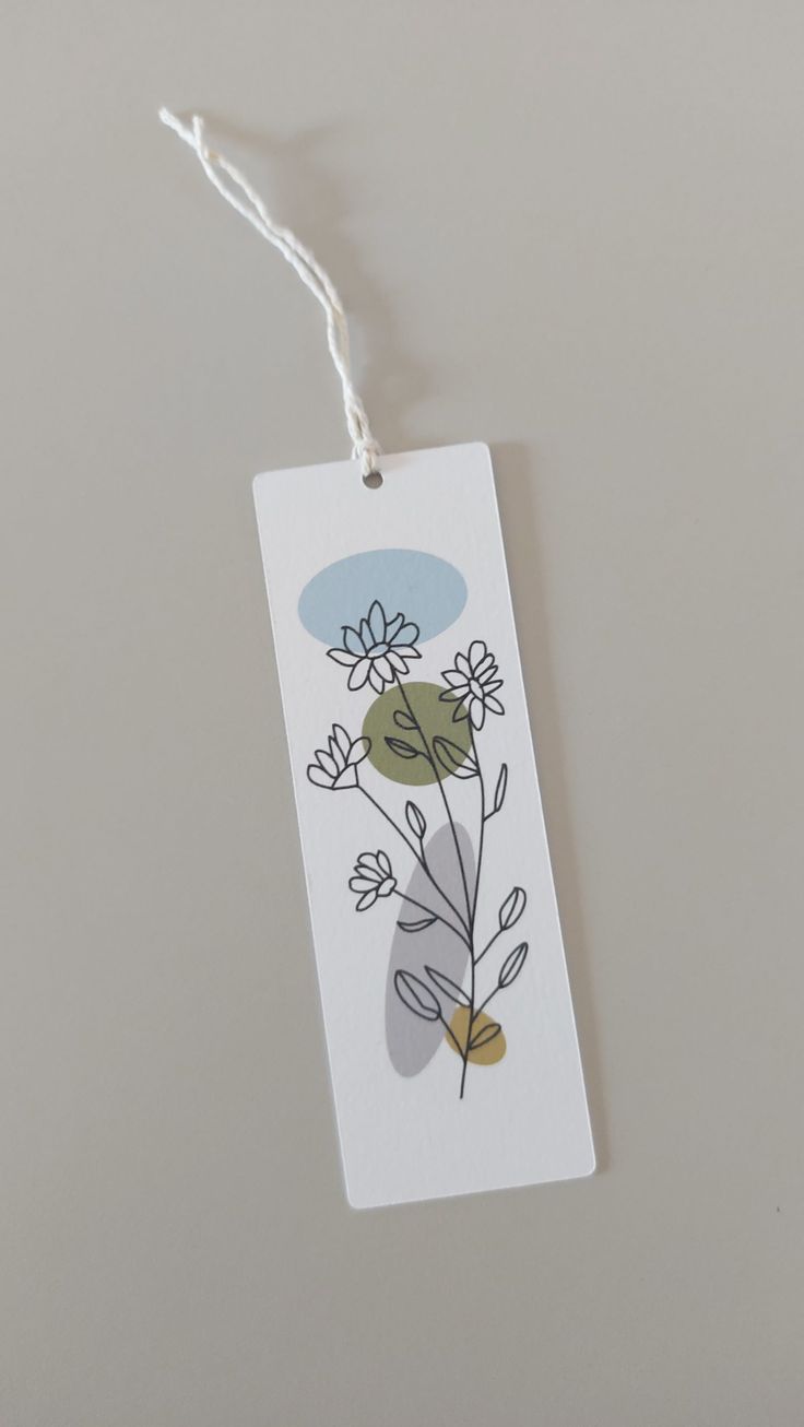 a white tag with flowers on it hanging from a string attached to a gray wall