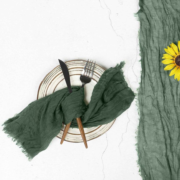 a plate with a fork, knife and green scarf next to a sunflower on a white wall