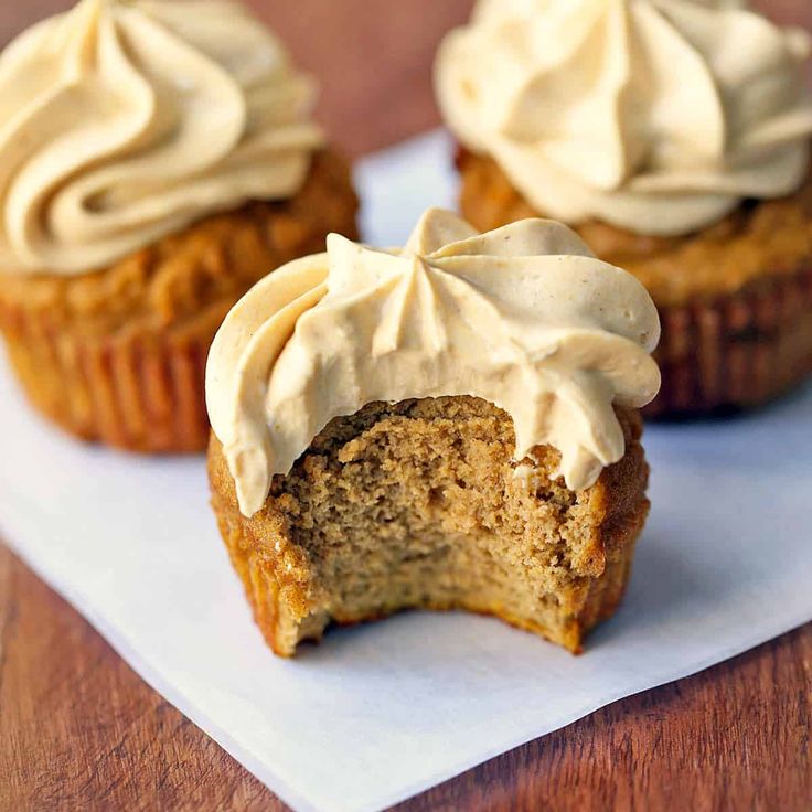 two pumpkin cupcakes with cream cheese frosting are on a white paper towel