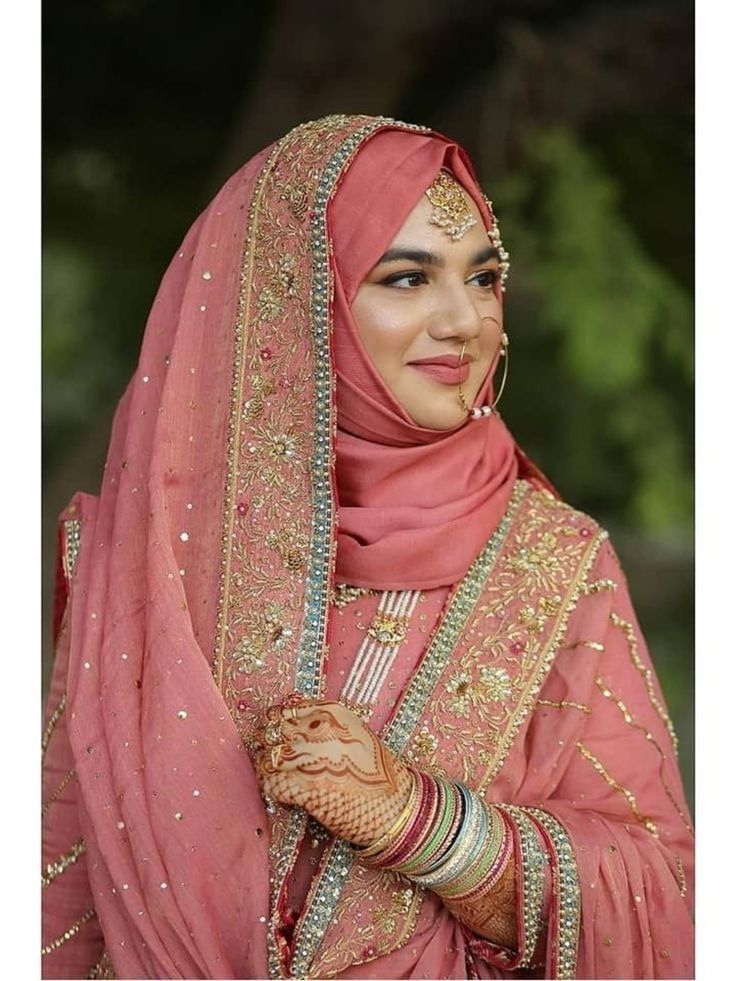 a woman wearing a pink veil and holding her hand up to her chest, smiling at the camera