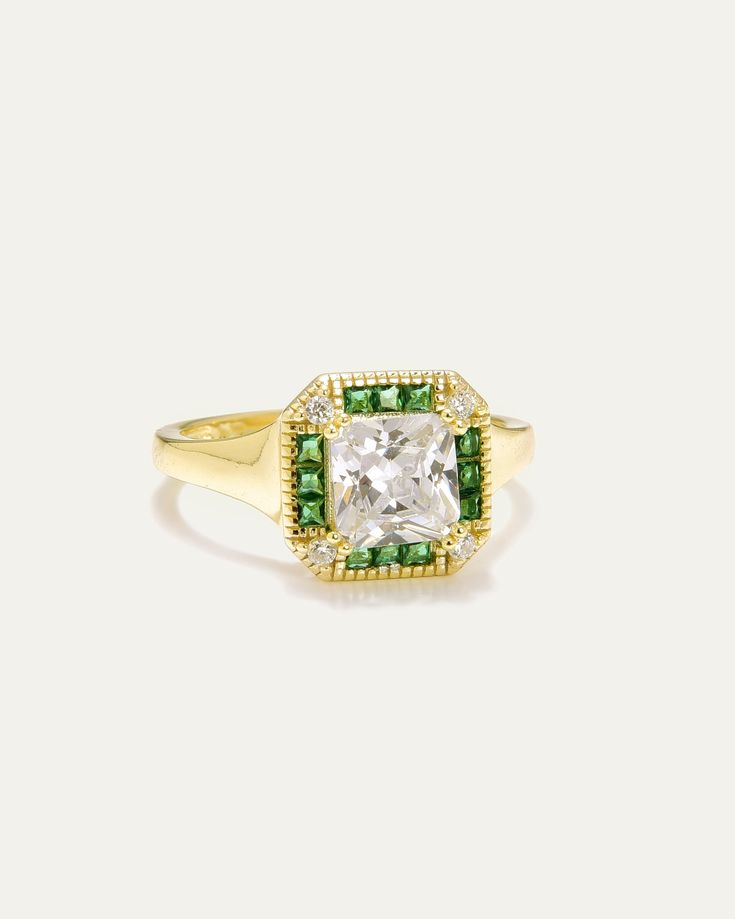 Introducing our Golden Regalia Art Deco Ring, a remarkable piece that exudes the sophisticated elegance of the Art Deco era. This sterling silver ring, plated in luxurious gold, is adorned with a stunning princess-cut clear cubic zirconia at its center. Encircling this radiant stone is a halo of green spinel baguettes, complemented by clear cubic zirconia accents, further enhancing the ring's exquisite charm. With Contessa Di Capri, step into a world of timeless elegance and modern flair. Deco Ring, Art Deco Era, Art Deco Ring, Princess Cut, Sterling Silver Ring, Timeless Elegance, Silver Ring, Sterling Silver Rings, Halo