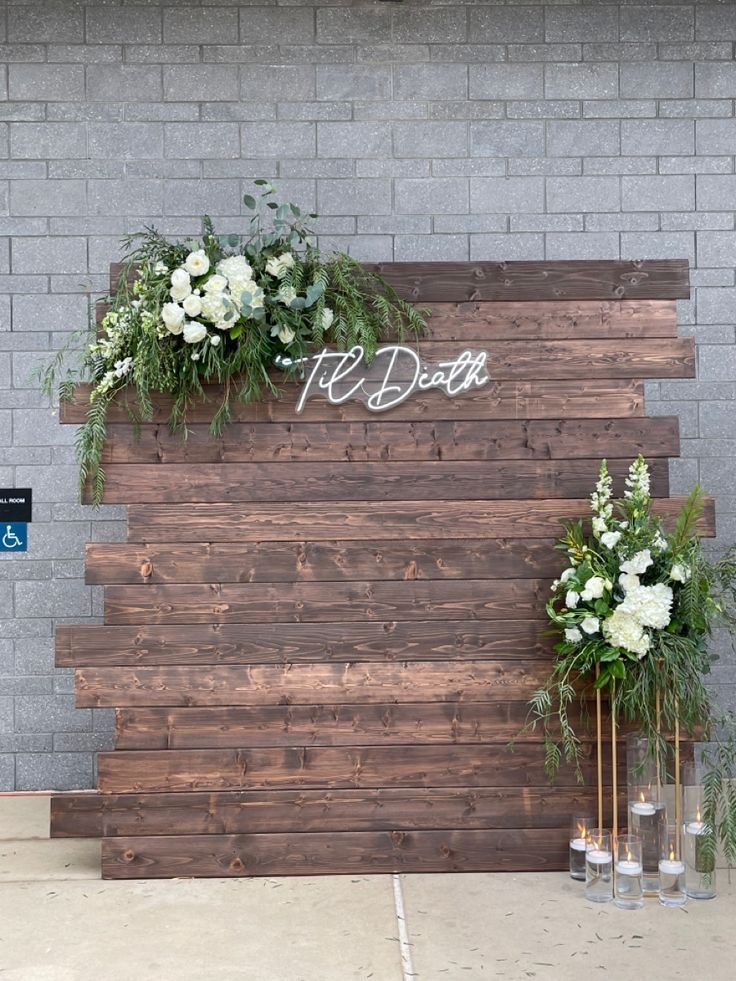 two vases filled with flowers and greenery on top of a wooden board wall