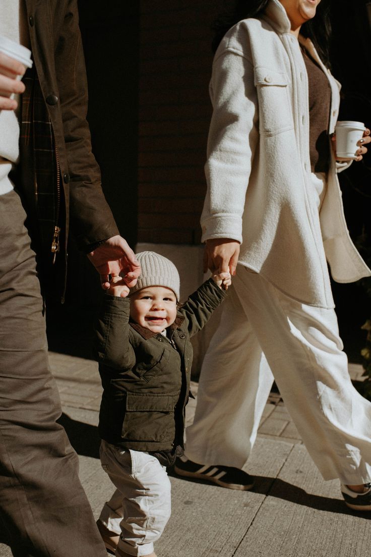 a small child is holding the hand of an older person as they walk down a sidewalk