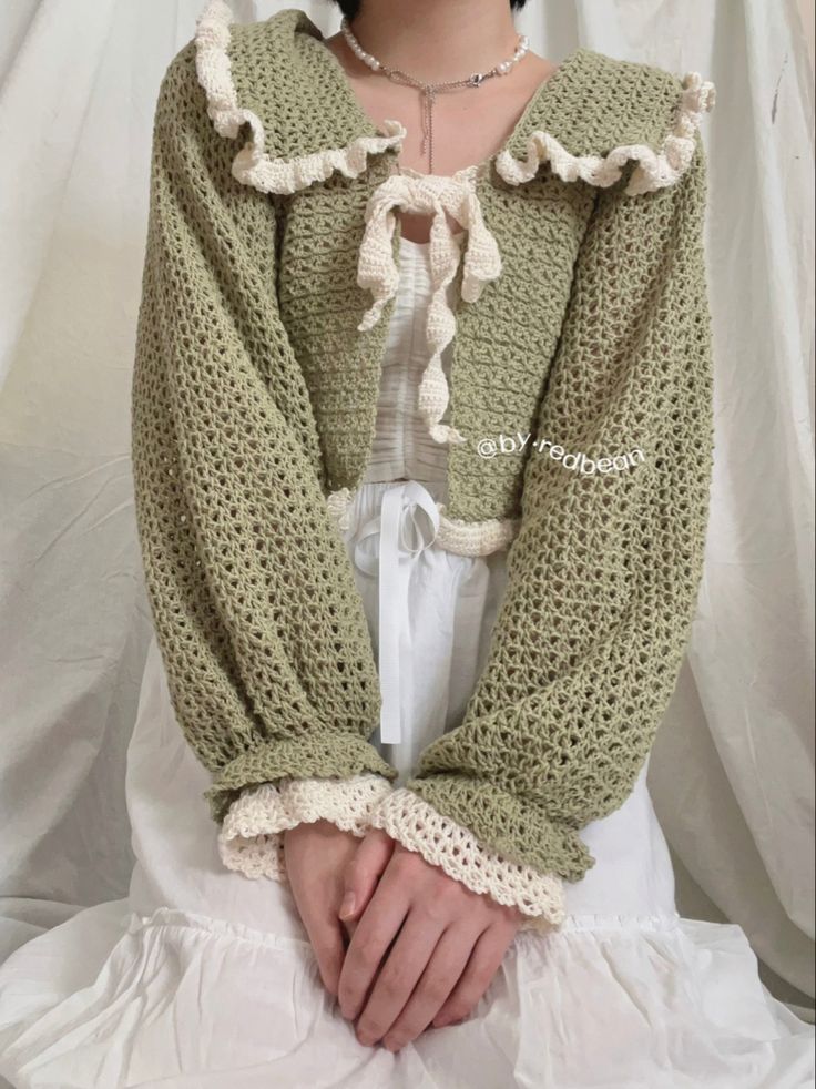 a woman wearing a green crochet jacket with ruffles on the sleeves