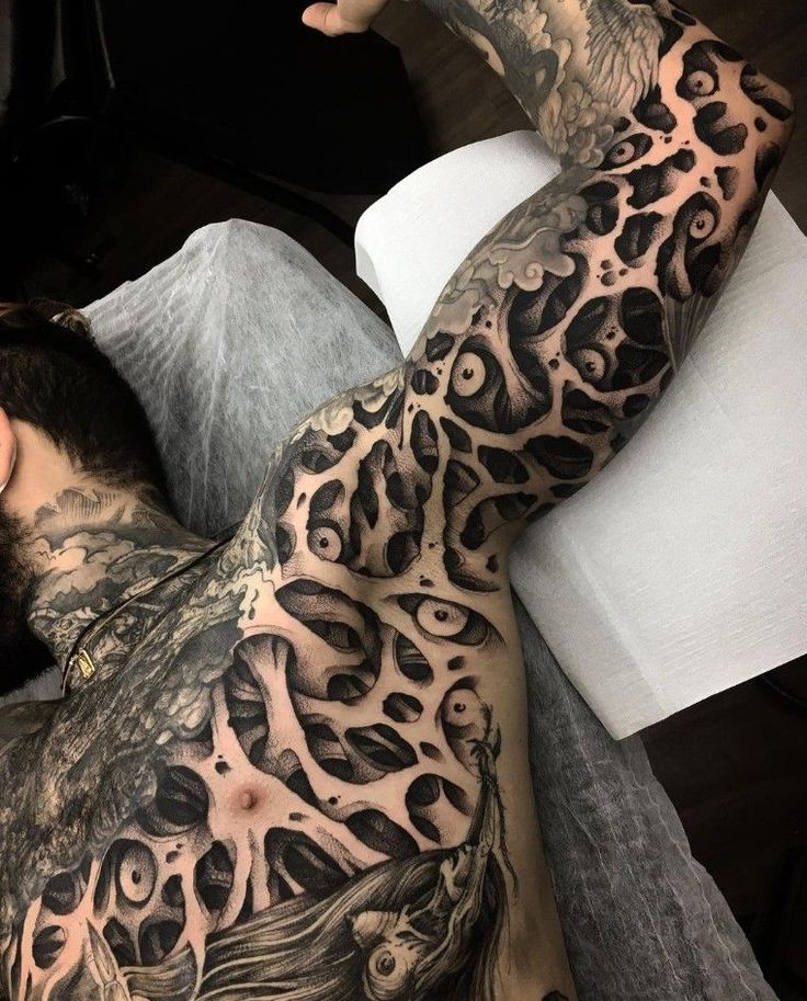 a man laying on top of a bed covered in lots of black and grey tattoos