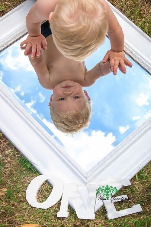 a toddler looking at himself in the reflection of a mirror on the ground with his hands up