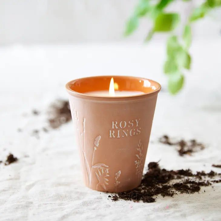 a candle that is sitting on some dirt next to a potted plant with the words rosy rings written on it