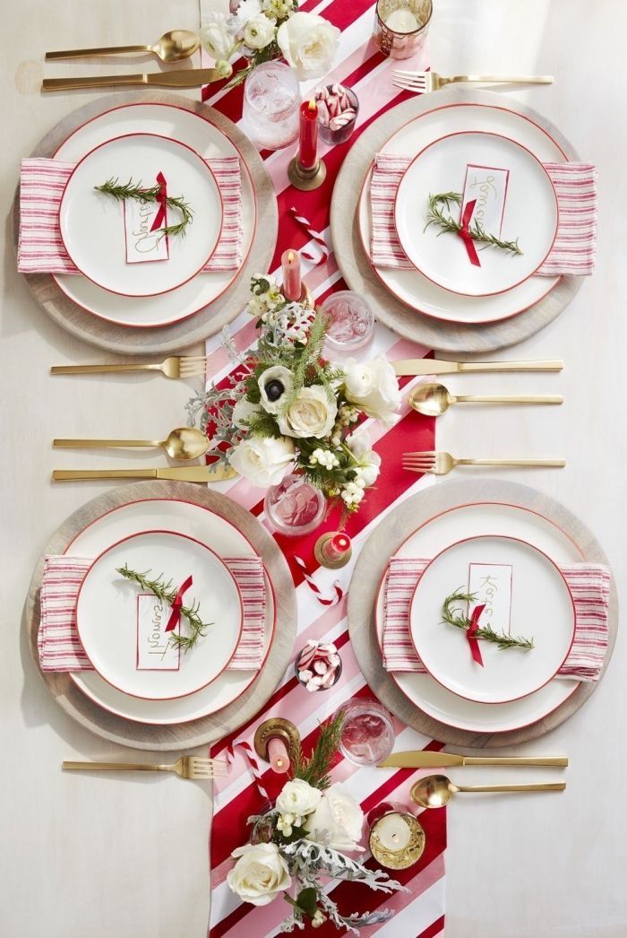 the table is set with red and white plates, silverware, flowers and greenery