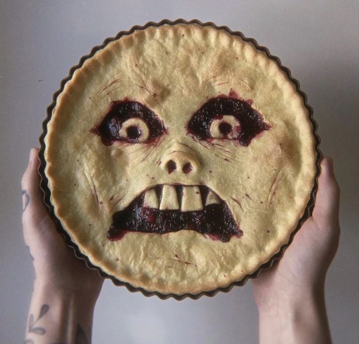 a person holding up a pie with an evil face on it's face and hands