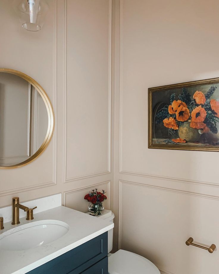 a white toilet sitting next to a bathroom sink under a framed flower painting on the wall