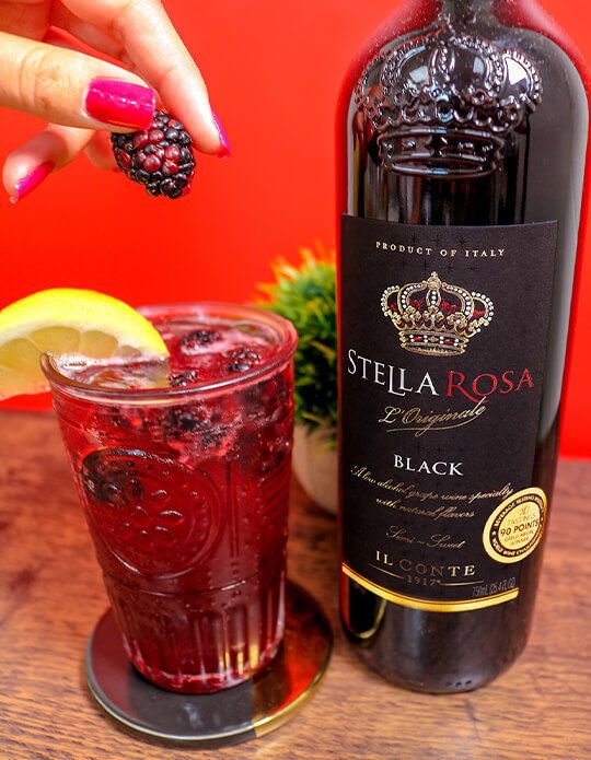 a bottle of stella rossa next to a glass filled with liquid and lemon wedges