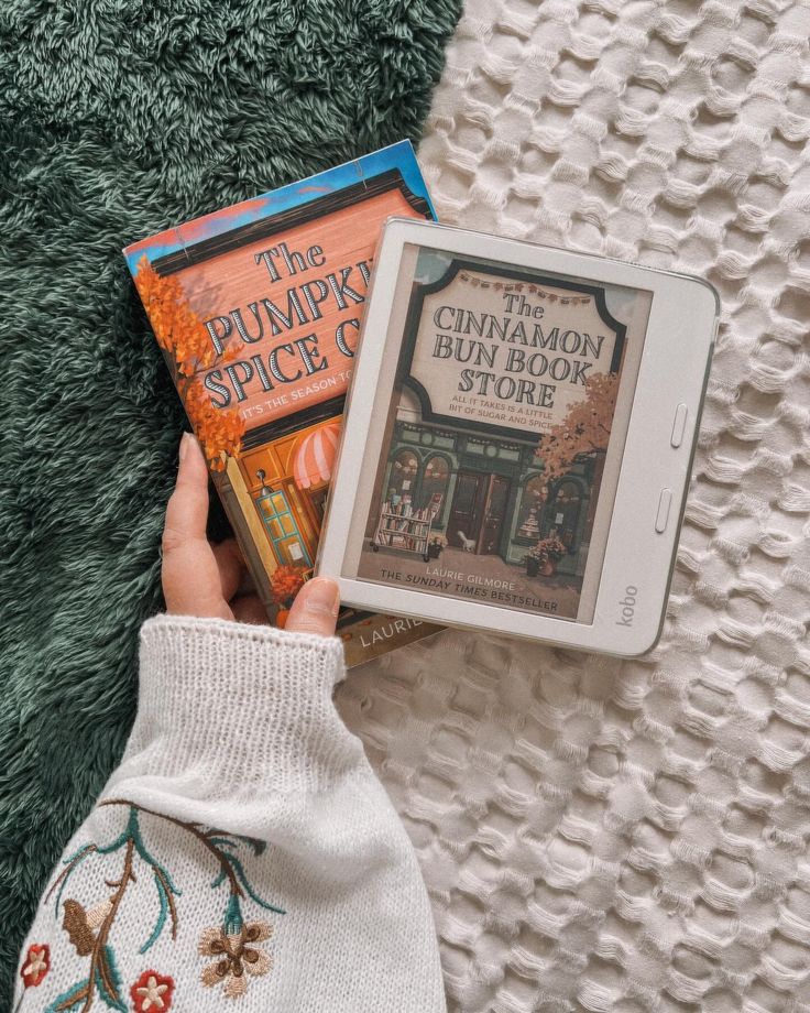 a person holding two books in their hands while laying on the floor next to a blanket