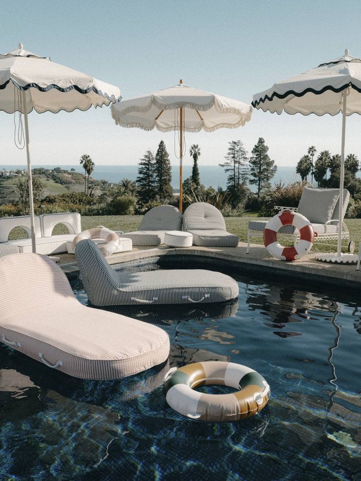 an outdoor pool with lounge chairs and umbrellas next to the swimming pool is shown