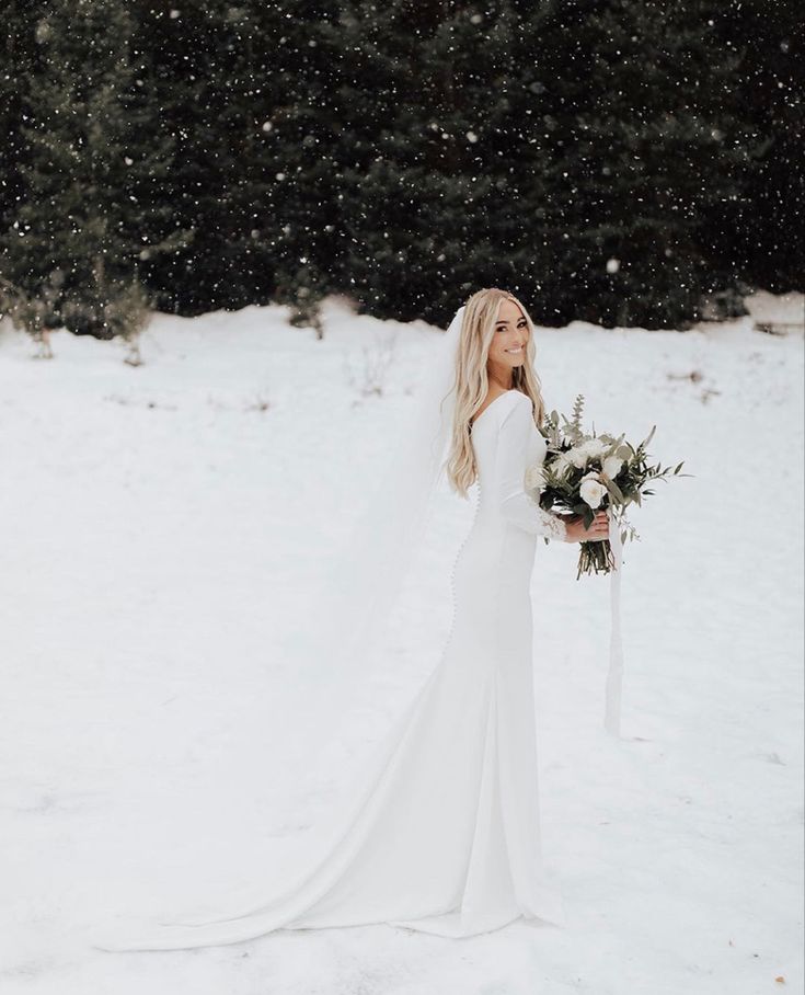 a woman in a wedding dress standing in the snow holding a bouquet and looking off into the distance