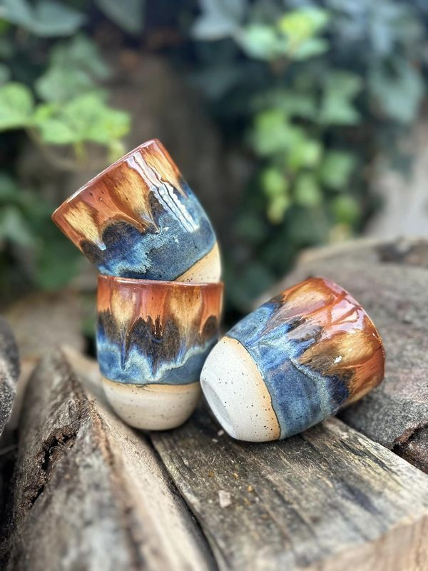 two ceramic cups sitting on top of a wooden table next to rocks and plants in the background