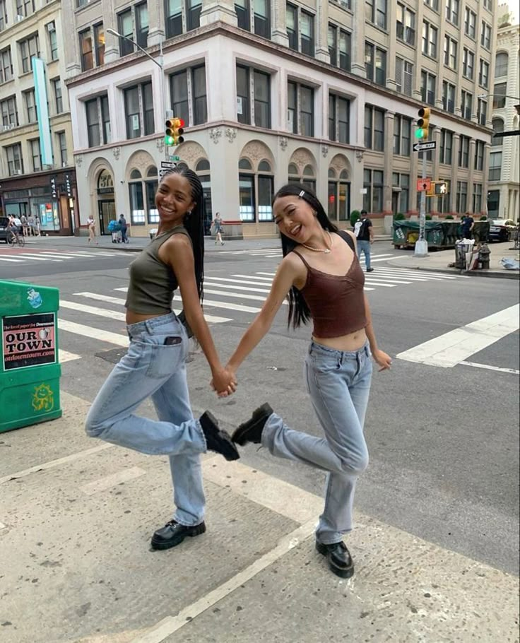 two young women holding hands while crossing the street