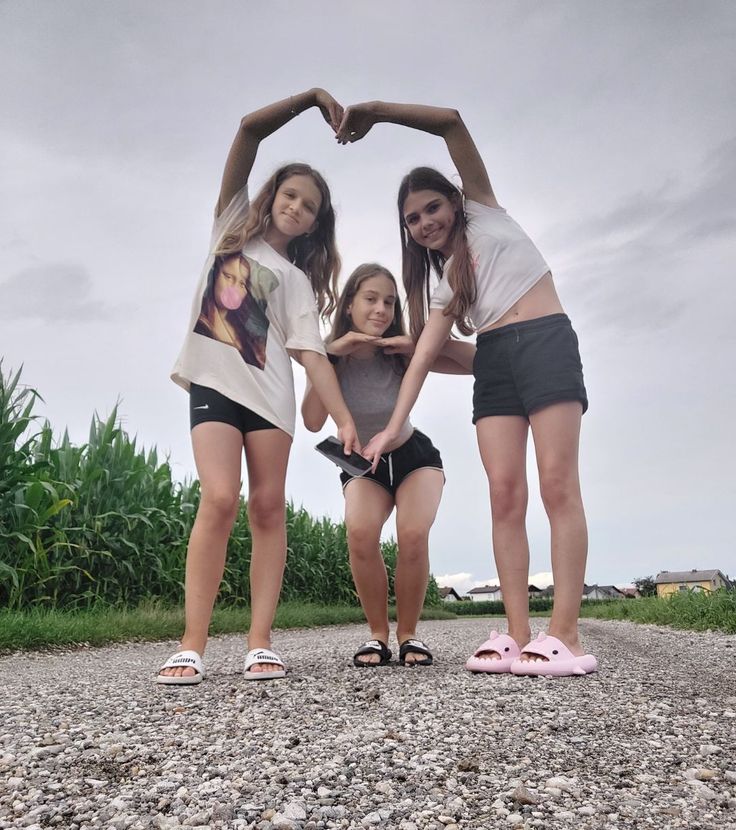 three girls standing in the middle of a gravel road making a heart shape with their hands