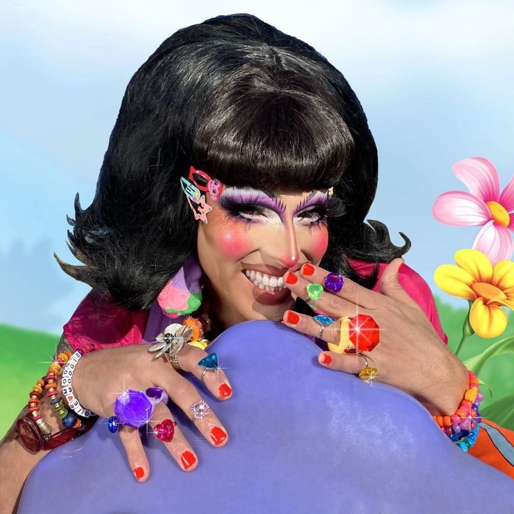 a woman with bright makeup holding onto a large object in front of flowers and grass