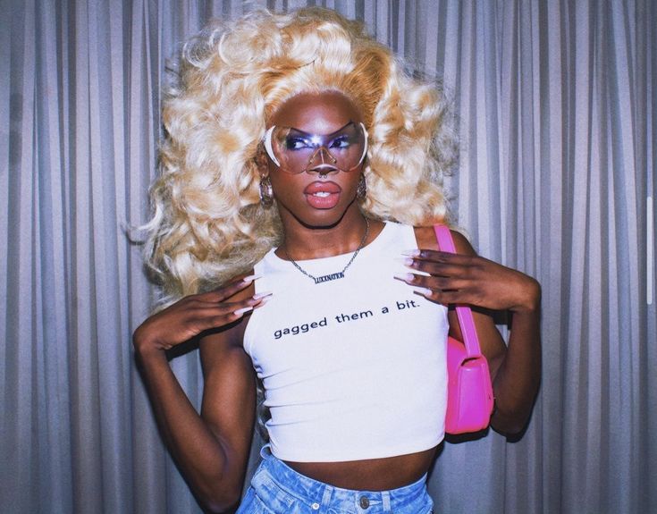 a woman with blonde hair and glasses holding a pink handbag in front of her face