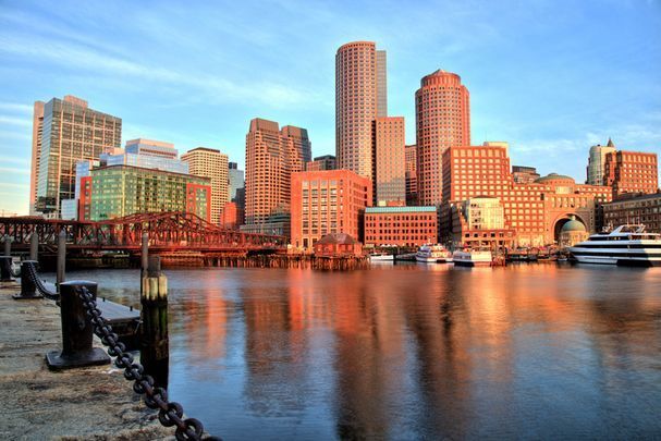 the city skyline is reflected in the water near a chain link fence that runs along the river