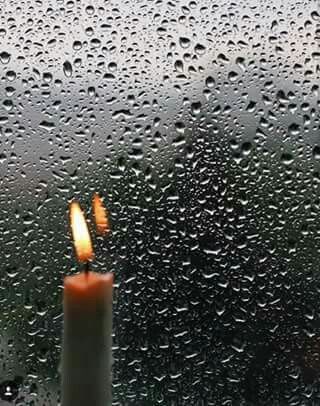 a candle sitting on top of a window covered in rain