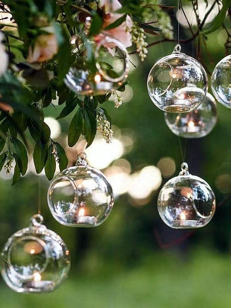 several glass ornaments hanging from a tree with white flowers in the background and greenery