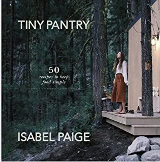 a woman standing on the porch of a tiny cabin in the woods with trees and rocks